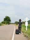 Woman with luggage hitchhiking along a road Royalty Free Stock Photo