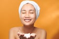 Young Asian woman showing foaming cleanser on her hand while wearing a bath towel over orange background