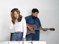 Young asian woman sing while playing an electric keyboard in front of white walls. Her boyfriend play the guitar together. Royalty Free Stock Photo