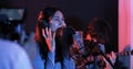 Young asian woman singing while man in background playing acoustic guitar. Royalty Free Stock Photo