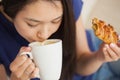 Young asian woman sipping her coffee and holding a pastry