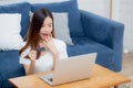 Young asian woman sit on sofa using laptop computer shopping online with credit card buy to internet and surprise. Royalty Free Stock Photo