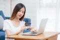 Young asian woman sit on sofa using laptop computer shopping online with credit card buying to internet happy girl payment with e Royalty Free Stock Photo