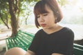 Young Asian woman sitting alone on the public bench in the park surrounded with nature and warm sunlight. Royalty Free Stock Photo