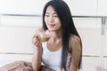 Young Asian woman sitting on a bed holding a cup of coffee Royalty Free Stock Photo