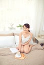 Young Asian woman sitting on the bed, reading a book and drink tea or coffee Royalty Free Stock Photo