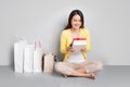 Young asian woman sitting besides row of shopping bags holding r Royalty Free Stock Photo