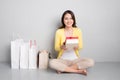 Young asian woman sitting besides row of shopping bags holding r Royalty Free Stock Photo