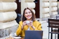 Young Asian woman sitting in coffee shop at wooden table, drinking coffee and using smartphone.On table is laptop. Girl browsing Royalty Free Stock Photo