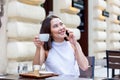 Young Asian woman sitting in coffee shop at wooden table, drinking coffee and using smartphone.On table is laptop. Girl browsing Royalty Free Stock Photo