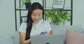 Young Asian woman sitting on couch using smartphone and laptop notebook looking at screen typing message. Happy girl Royalty Free Stock Photo