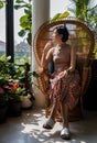 A young asian woman sitting and relax on peacock wicker rattan chair near glass window in living room Royalty Free Stock Photo