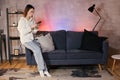 Young asian woman sitting on a sofa in a cozy room looks at the phone