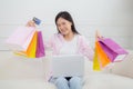 Young asian woman sitting on sofa using laptop computer shopping online with credit card and holding paper bag. Royalty Free Stock Photo