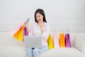 Young asian woman sitting on sofa using laptop computer shopping online with credit card and holding paper bag. Royalty Free Stock Photo