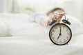 Young asian woman sleeping on bed pressing snooze button on black vintage alarm clock at seven o`clock morning in bed room at hom