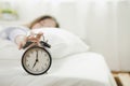 Young asian woman sleeping on bed pressing snooze button on black vintage alarm clock at seven o`clock morning in bed room at hom Royalty Free Stock Photo