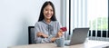 Young asian woman smiling and holding credit card while using laptop for online shopping Royalty Free Stock Photo