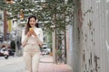 Young Asian woman smiling looking at mobile phone wearing headphones and long sleeves sweater while walking down the street Royalty Free Stock Photo