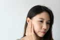 Young Asian woman with sore ear suffering from otitis over white background. Girl touch her ear with pain. Ear problem