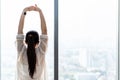 Young asian woman standing in front of big window, stretching arms and back, enjoying good morning time in office. Royalty Free Stock Photo