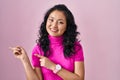 Young asian woman standing over pink background pointing to the back behind with hand and thumbs up, smiling confident Royalty Free Stock Photo