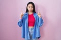 Young asian woman standing over pink background pointing up looking sad and upset, indicating direction with fingers, unhappy and Royalty Free Stock Photo