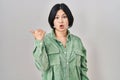 Young asian woman standing over white background surprised pointing with hand finger to the side, open mouth amazed expression Royalty Free Stock Photo