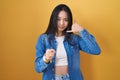 Young asian woman standing over yellow background smiling doing talking on the telephone gesture and pointing to you Royalty Free Stock Photo