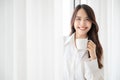 Young asian woman standing beside window and holding mug in bedroom at home Royalty Free Stock Photo