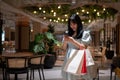 A young Asian woman stands in the shopping mall, holding shopping bags and looking at her phone Royalty Free Stock Photo