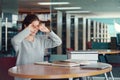 Young Asian woman student rubbing eyes, feeling tired after reading a book in library Royalty Free Stock Photo