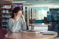 Young Asian woman student rubbing eyes, feeling tired after reading a book in library Royalty Free Stock Photo