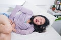 Young Asian woman suffering menses abdominal cramp - sick and tired Chinese girl lying on bed having having period pain holding Royalty Free Stock Photo