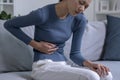 Young Asian woman suffering from strong abdominal pain while sitting on sofa at home. Royalty Free Stock Photo