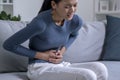 Young Asian woman suffering from strong abdominal pain while sitting on sofa at home. Royalty Free Stock Photo