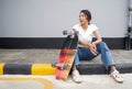 Young asian woman with sunglasses on her head resting after skateboarding. The skateboard is placed on the edge of the pedestrian Royalty Free Stock Photo