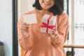 Young asian woman in sweater holding striped gift box with red ribbon and blank wishing card Royalty Free Stock Photo