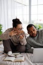 Young asian woman in sweater talking to african american boyfriend near laptop and books on bed during online education Royalty Free Stock Photo