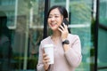 Young Asian woman talking on cell phone with coffee cup on background outside office Royalty Free Stock Photo