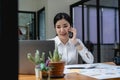 young asian woman talking on the mobile phone and smiling while sitting at her working place in office. Royalty Free Stock Photo