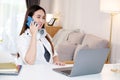 Young asian woman talking mobile phone while working with laptop computer, work at home, online learning Royalty Free Stock Photo