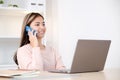 Young asian woman talking mobile phone while working with laptop computer, work at home, online learning Royalty Free Stock Photo