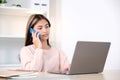 Young asian woman talking mobile phone while working with laptop computer, work at home, online learning Royalty Free Stock Photo