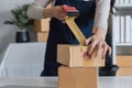Young asian woman taping up a cardboard box in home office SME e-commerce business, relocation and new small business Royalty Free Stock Photo