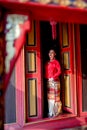 Young Asian woman with Thai Lanna traditional dress stand at door with red color and old style of ancient house also look to left Royalty Free Stock Photo