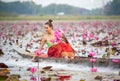 Young Asian women in Traditional dress in the boat and pink lotus flowers in the pond.