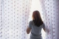 Young asian woman unveil curtain and looking out of window