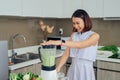 Young Asian woman using blender to make green smoothie in kitchen Royalty Free Stock Photo