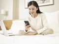 Young asian woman using cellphone and laptop on bed Royalty Free Stock Photo